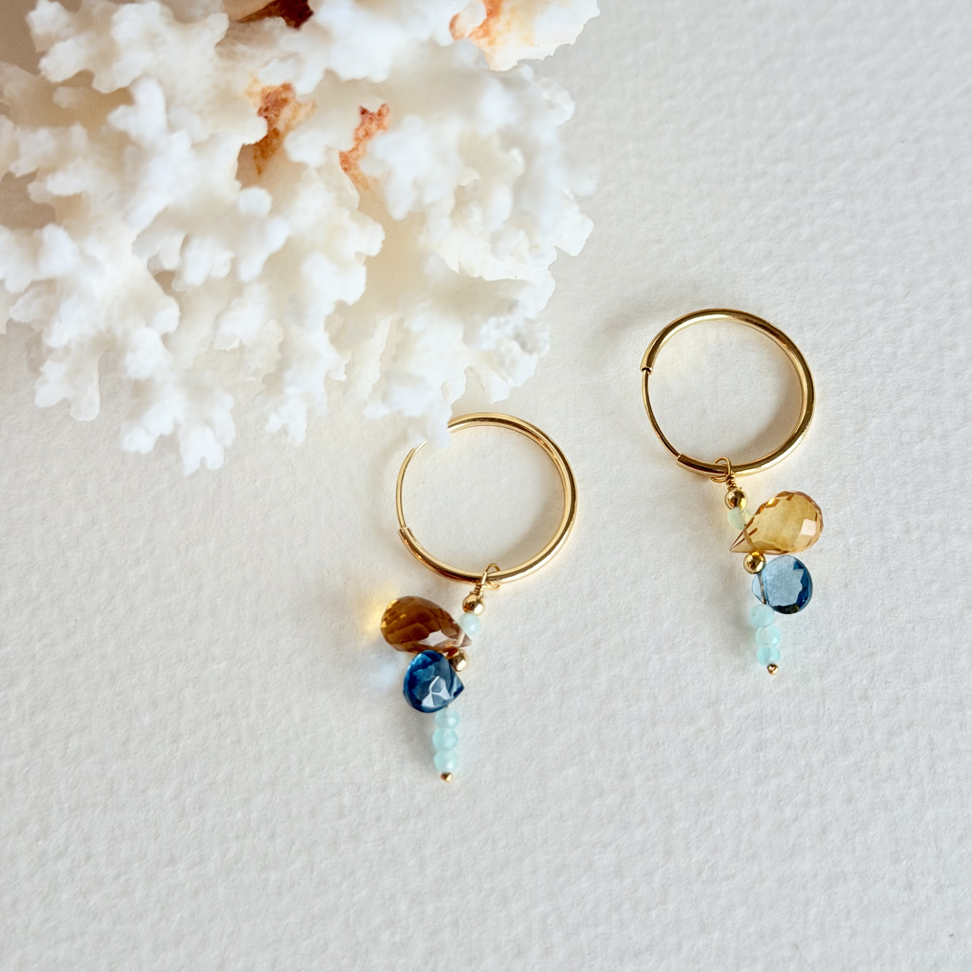 Gold hoop earrings with gemstone drops on a textured white surface