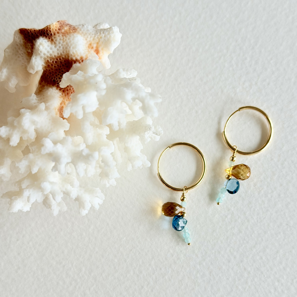Gold hoop earrings with beads on a textured white surface
