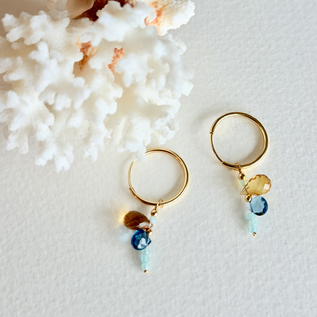 Gold hoop earrings with gemstone drops on a textured white surface