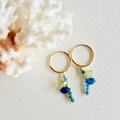 Gold hoop earrings with blue and green beads on a textured white background