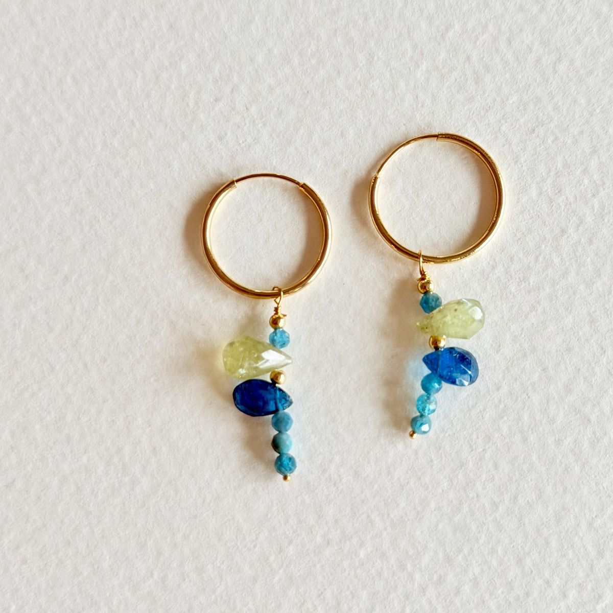 Pair of gold hoop earrings with blue and green beads on a light background
