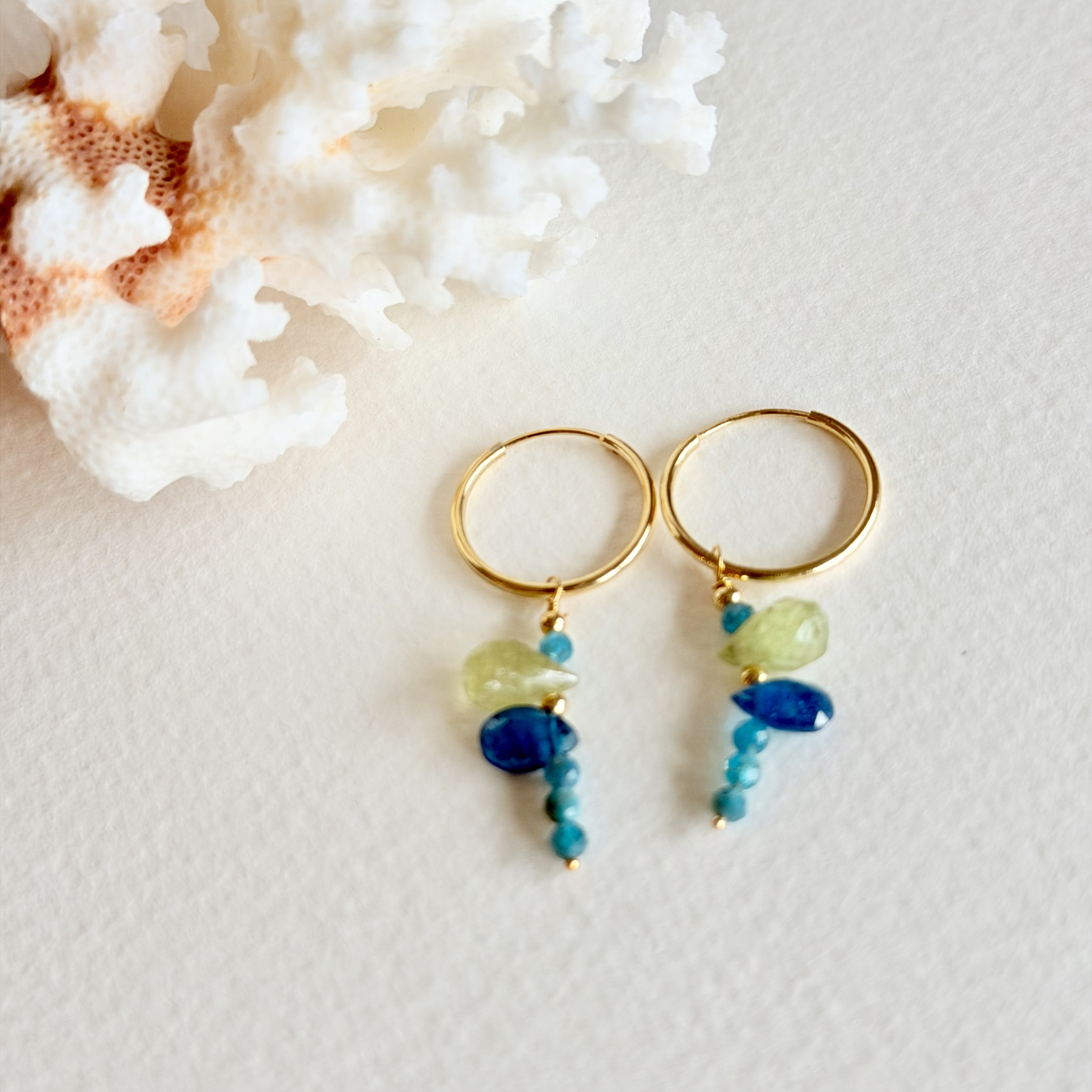 Gold hoop earrings with blue and green beads on a textured white surface.