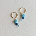 Gold hoop earrings with blue beads on a light gray background