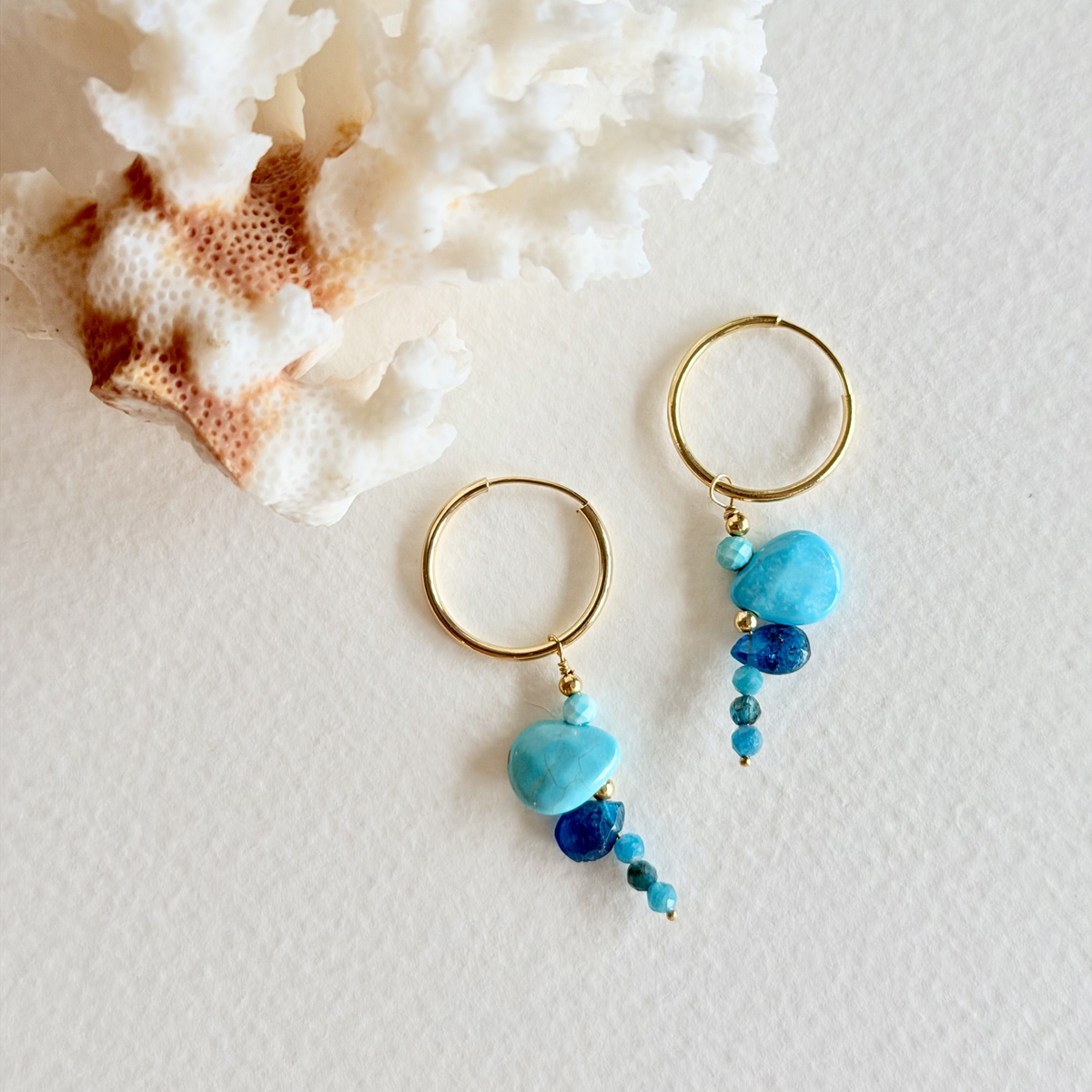Gold hoop earrings with blue beads on a textured white surface