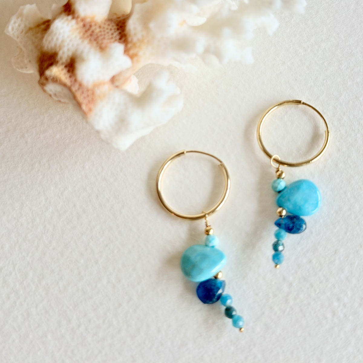Gold hoop earrings with blue beads on a textured white surface