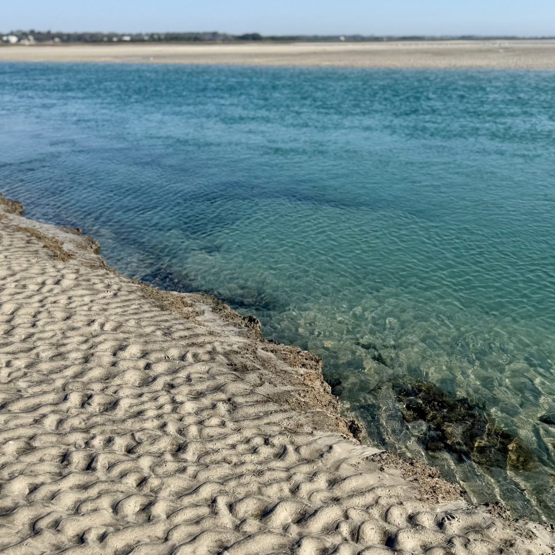 Clear blue water at a beach with textured sand in the foreground
