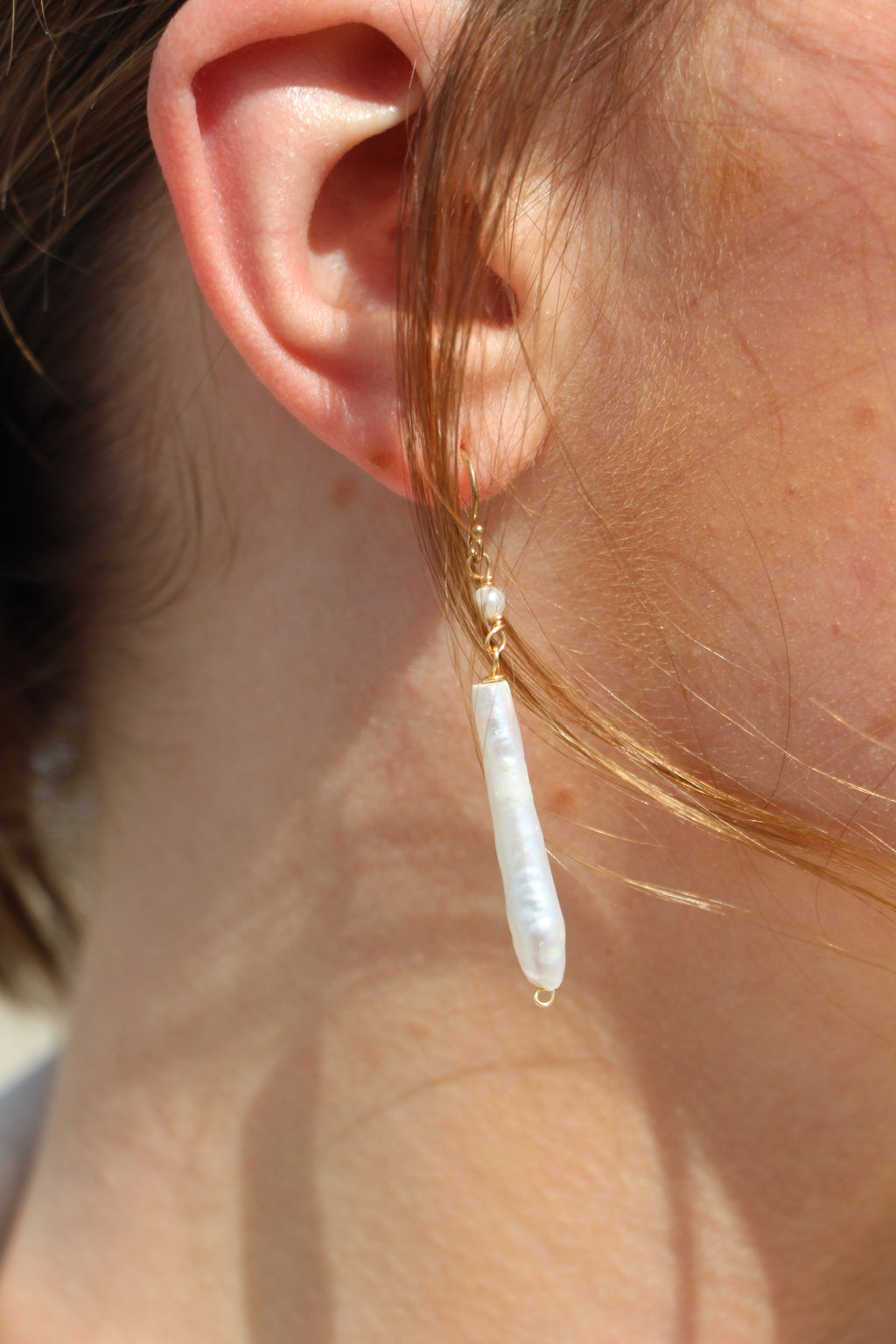 Close-up of an ear wearing a gold earring with a pearl drop.
