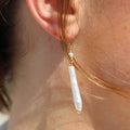 Close-up of an ear wearing a gold earring with a pearl drop.