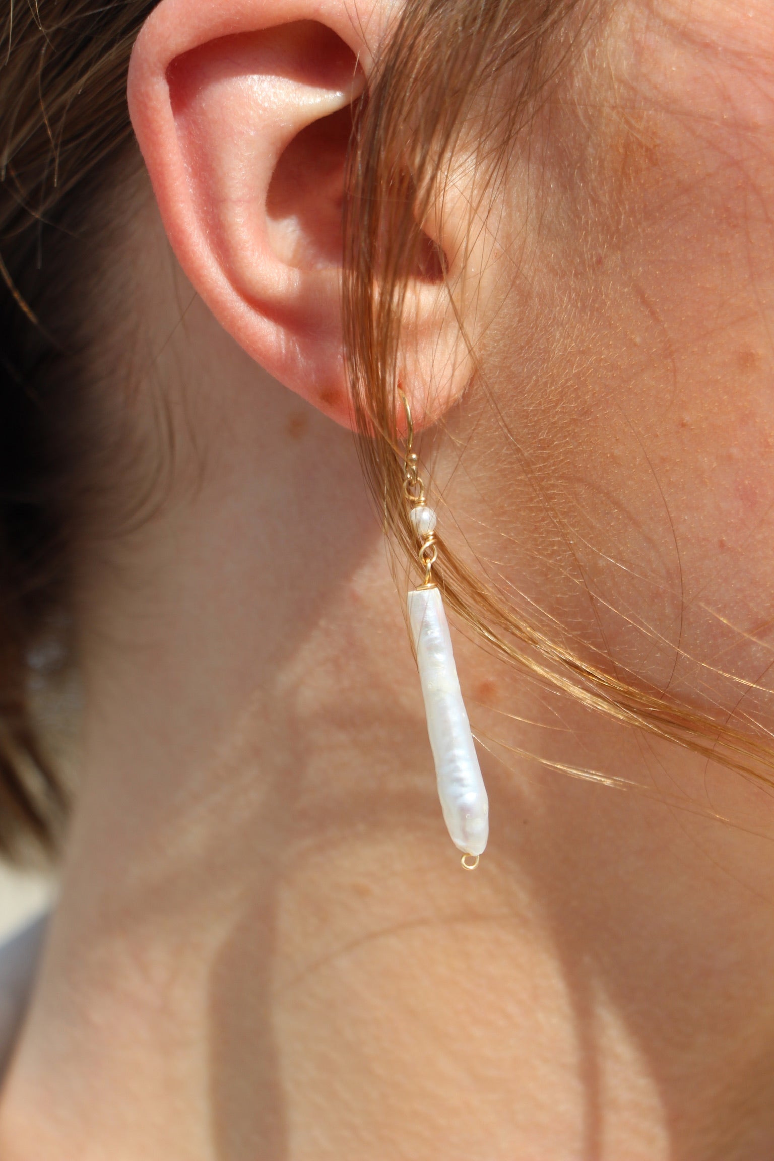 Close-up of an ear wearing a gold earring with a pearl drop.