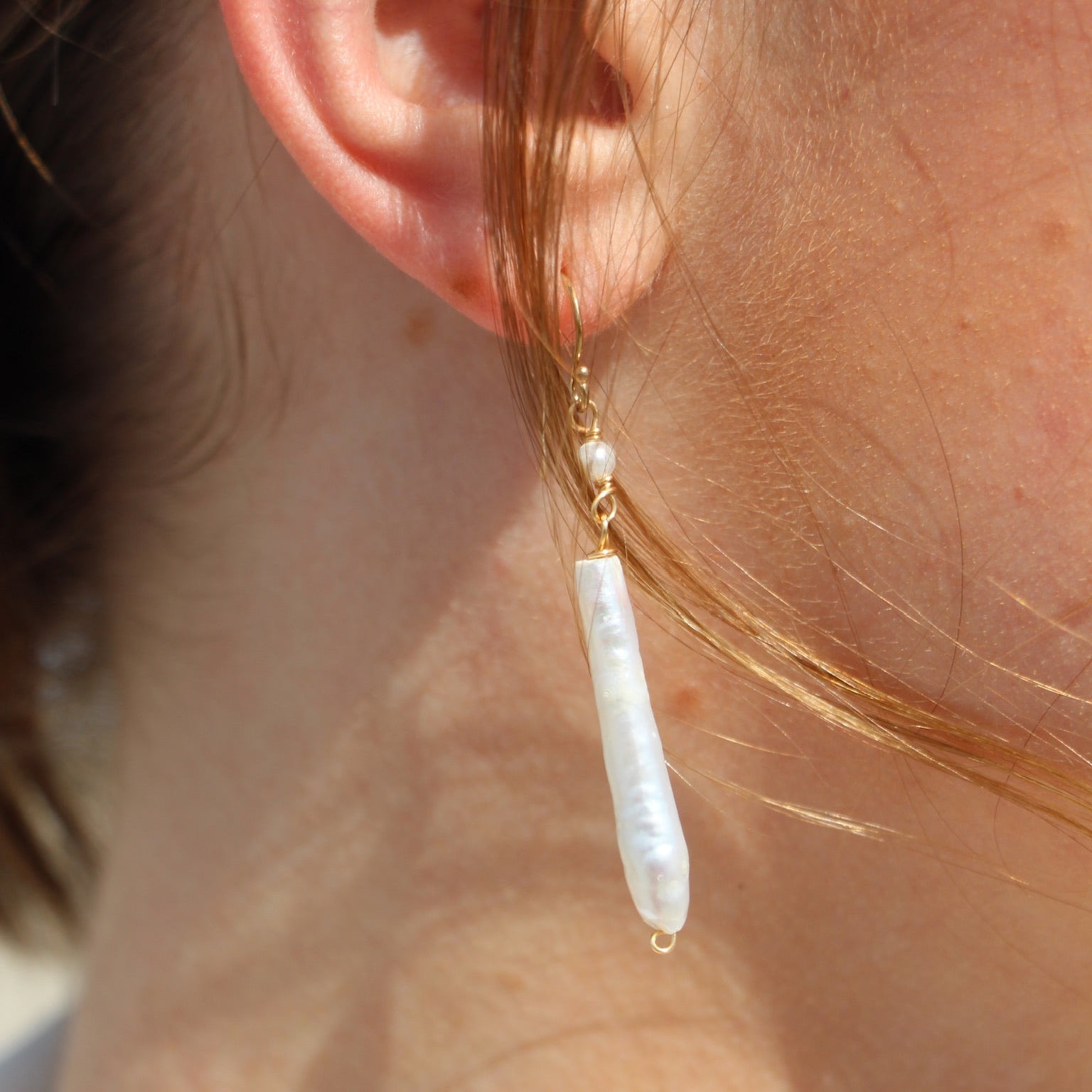 Close-up of an ear wearing a gold earring with a pearl drop.