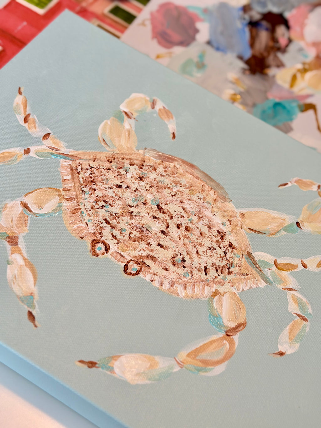 Close-up of whimsical blue crab acrylic artwork featuring textured coral and peach brushstrokes, delicate claws, and a turquoise background.