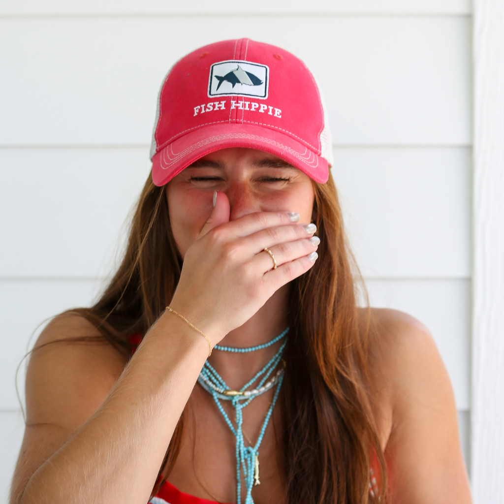 candid shot of model in a baseball hat laughing wearing Marie & Oakley jewelry
