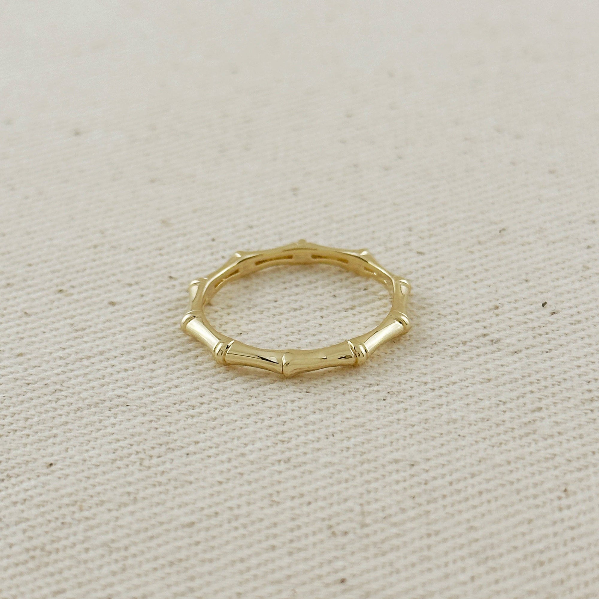 Gold ring with a bamboo design on a beige fabric background