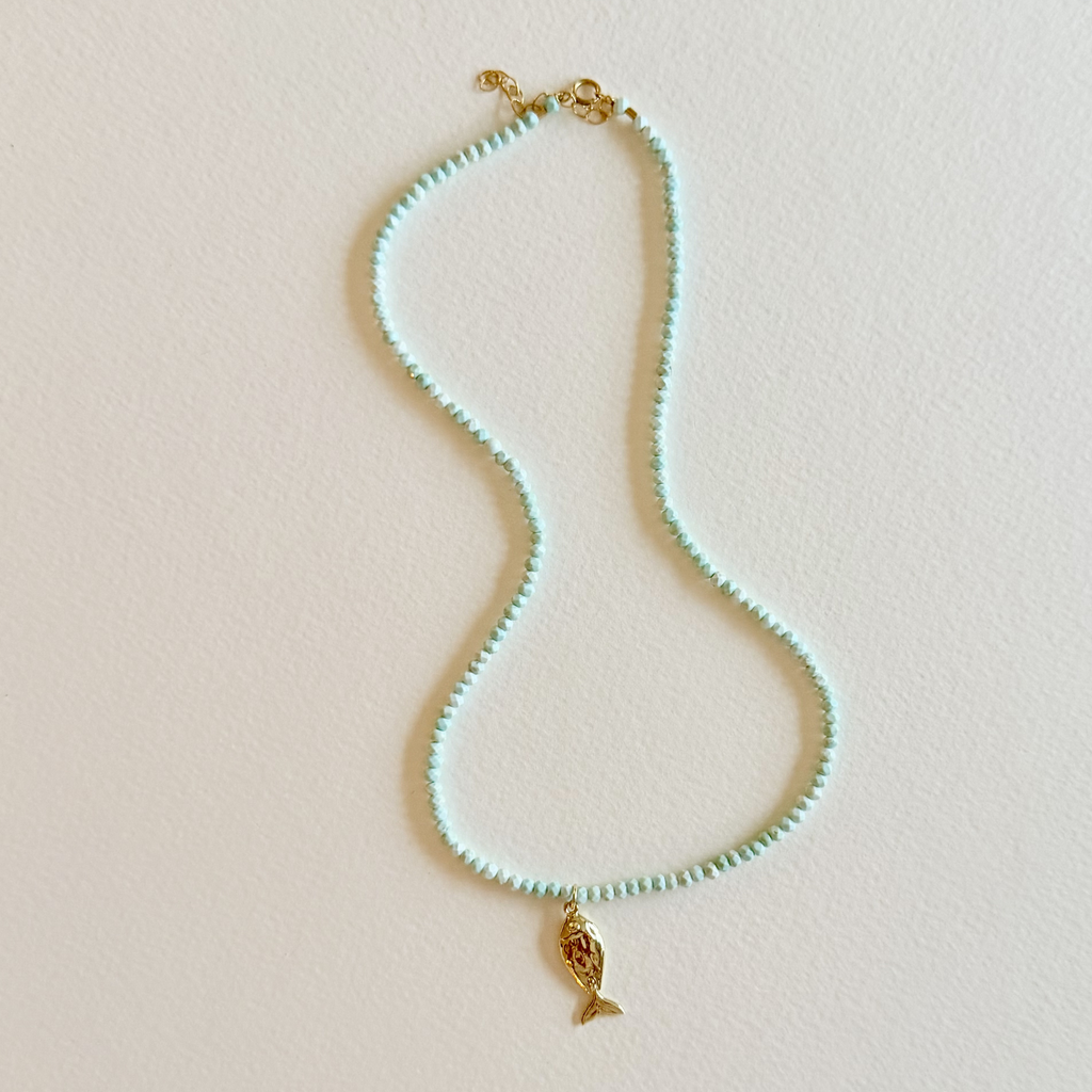 Handmade aqua turquoise beaded necklace with a signature gold fish charm and 14k gold-filled clasp, measuring 16 inches with a 2-inch extender. Inspired by the colors of the sea and handcrafted by Marie & Oakley.
