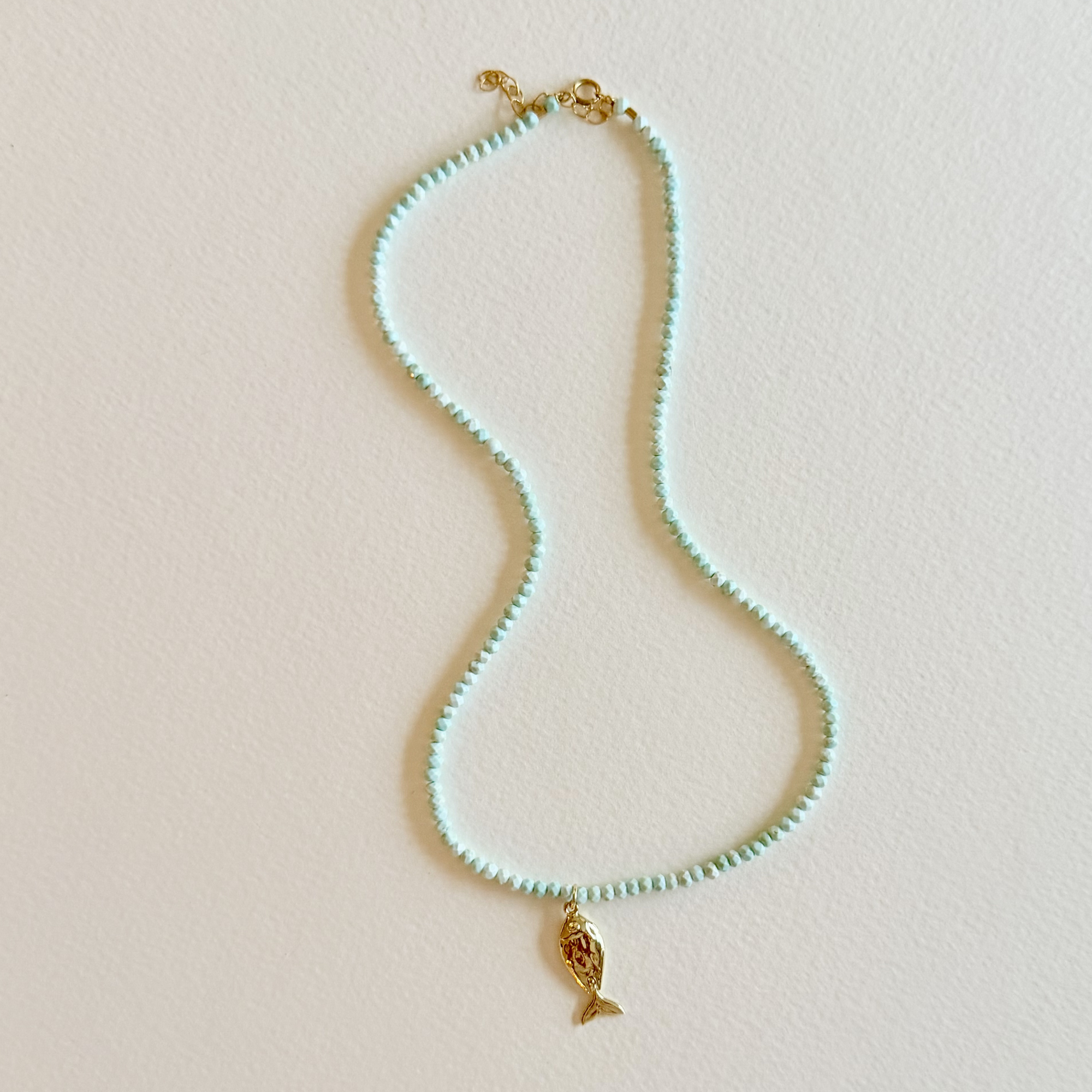 Handmade aqua turquoise beaded necklace with a signature gold fish charm and 14k gold-filled clasp, measuring 16 inches with a 2-inch extender. Inspired by the colors of the sea and handcrafted by Marie & Oakley.