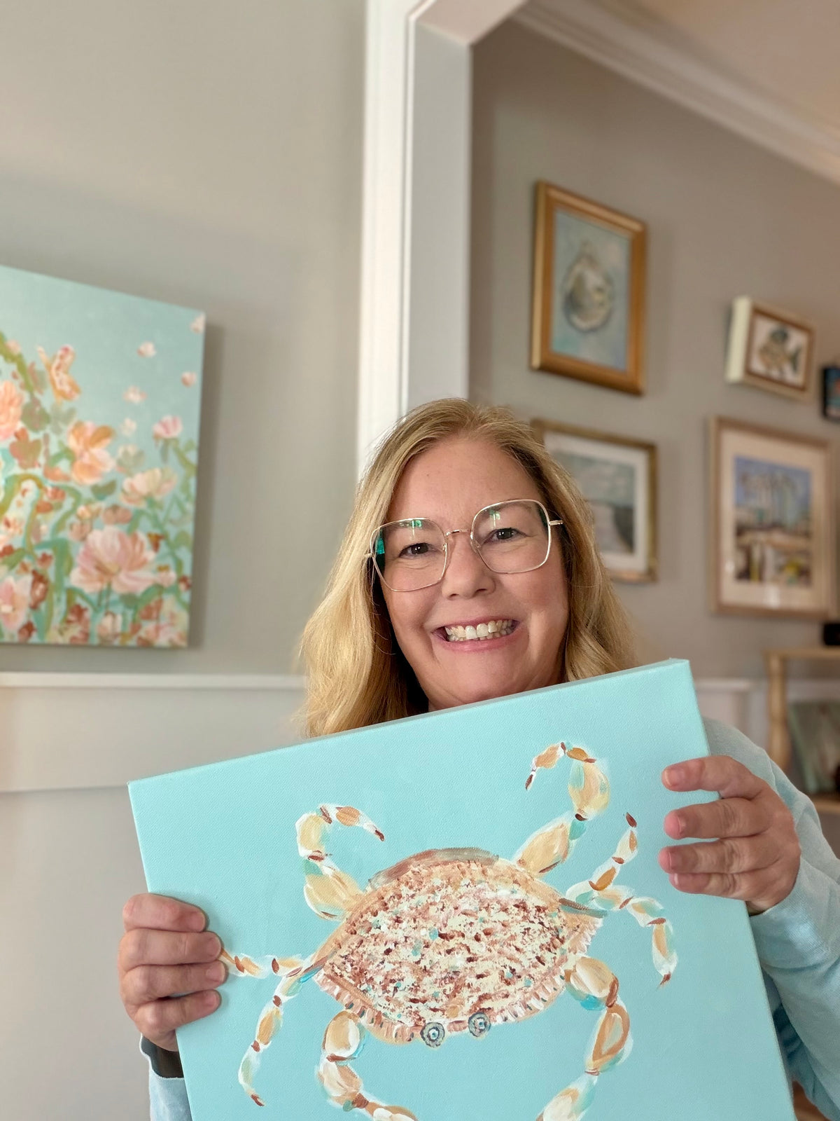 Marie & Oakley artist Tracy Grogan holding an original coastal blue crab painting in her Wilmington studio.
